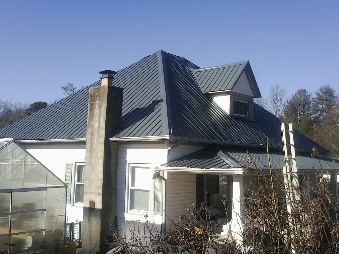 Dark blue standing seam metal roof on a white farmhouse with dormer — Slate & Tile Roof Repair by Roofing Brothers in Ambrose