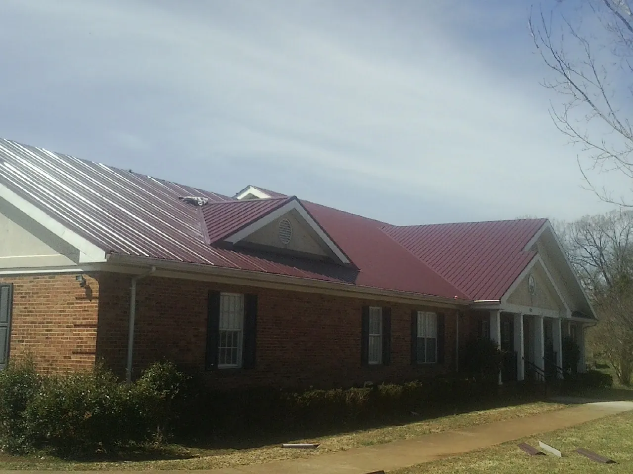 Red metal roof with gabled entries on a long brick building, from a Hail Damage Roof Repair job in Ambrose