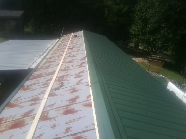 Old rusted panels beside newly installed green metal roofing — Wind Damage Roof Repair by Roofing Brothers in Ambrose