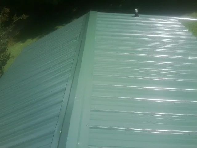 New green metal panels meeting at the ridge of a roof — Flat Roof Repair work by our crew in Ambrose