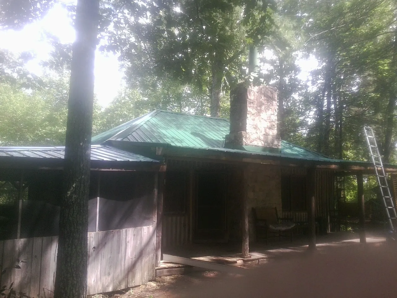 Green metal roof and stone chimney above a log cabin porch in Ambrose