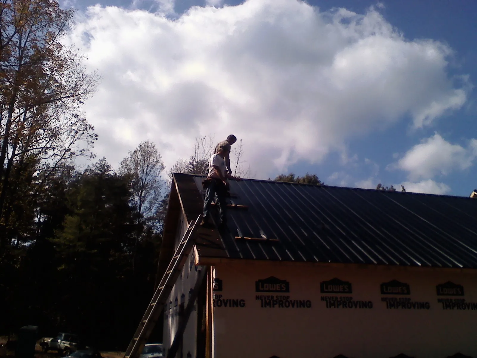 Roofer fastening dark metal panels high against a cloudy sky, from a Roof Inspection job in Ambrose