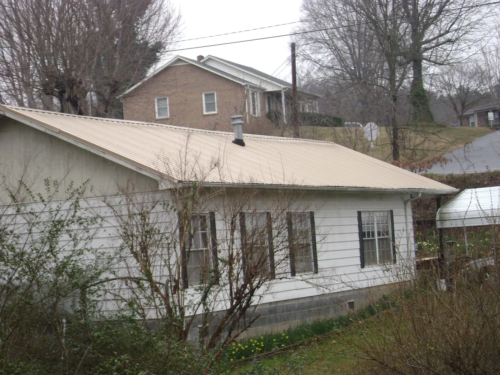 Tan metal roof on a white sided house set into a hillside — Commercial Roofing by Roofing Brothers in Ambrose