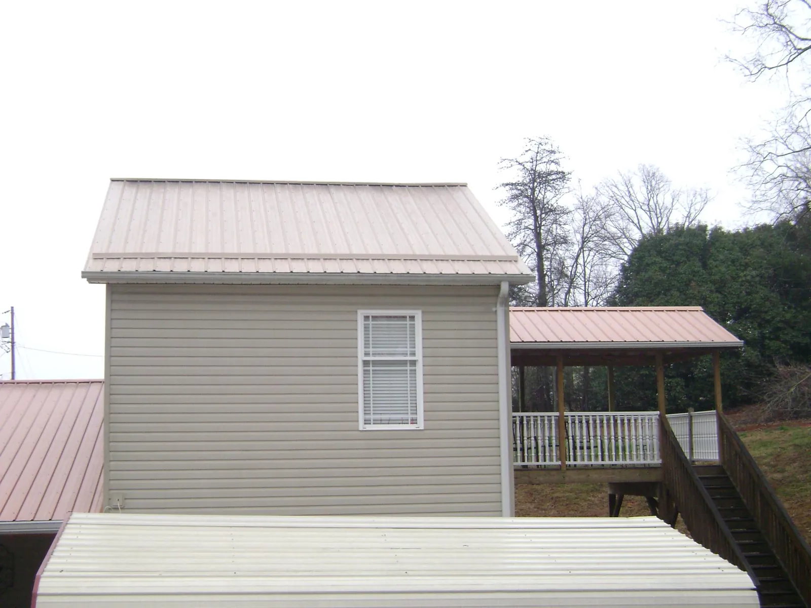 Tan metal roofs on a two story addition and attached porch, from a Roof Replacement job in Ambrose